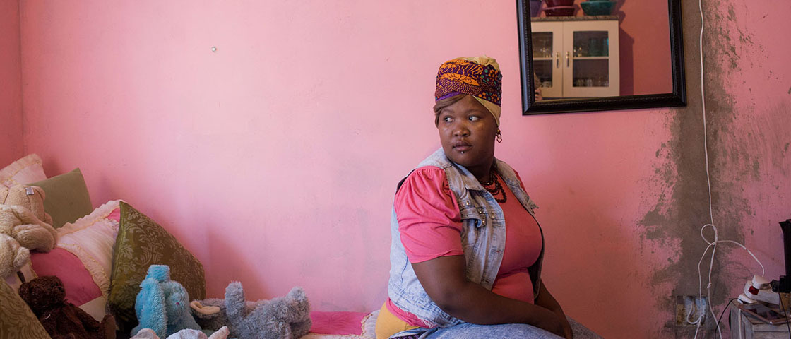A woman sitting in a pink-walled room looking over her shoulder to her side