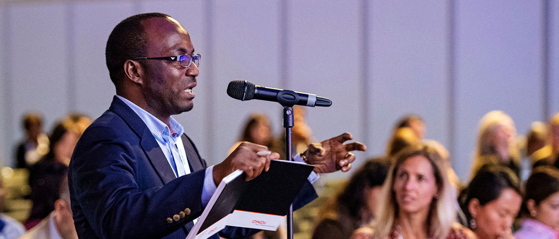A person holding a notebook speaks into a microphone