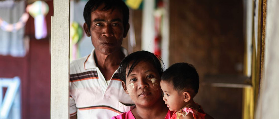 A man and woman stand in a doorway facing forward while the woman holds a young infant
