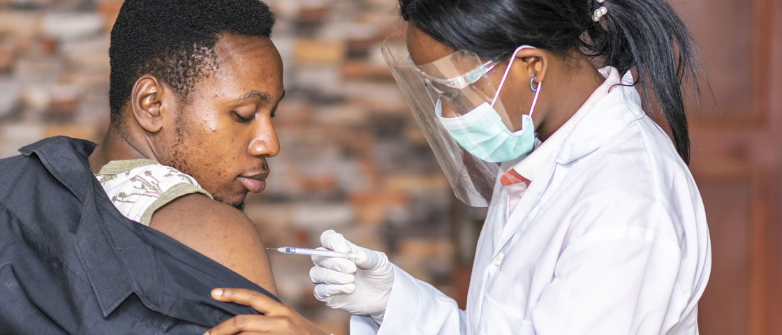 Clinician wearing a facemask administering a vaccination to a male patient