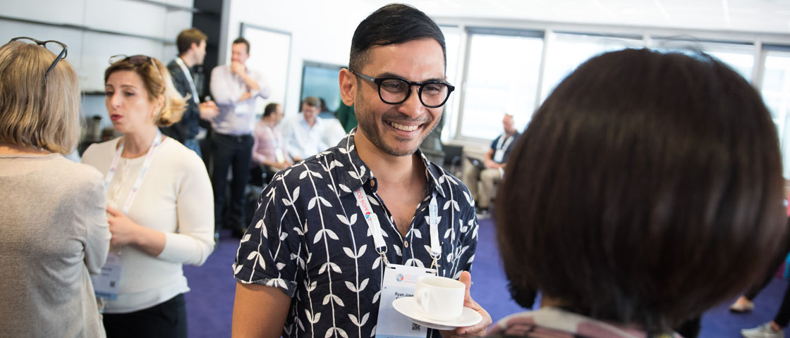Person at networking event holding a teacup smiles at a person facing them