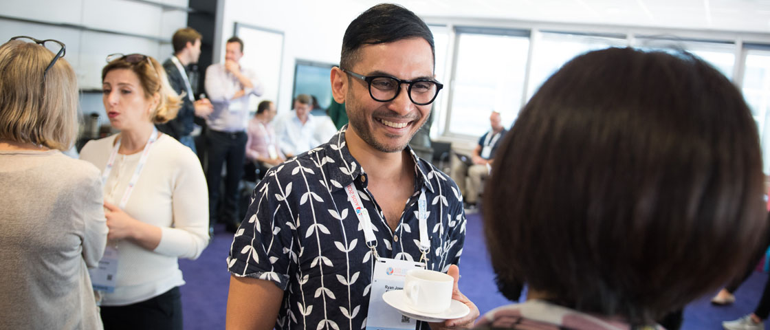 Person at networking event holding a teacup smiles at a person facing them