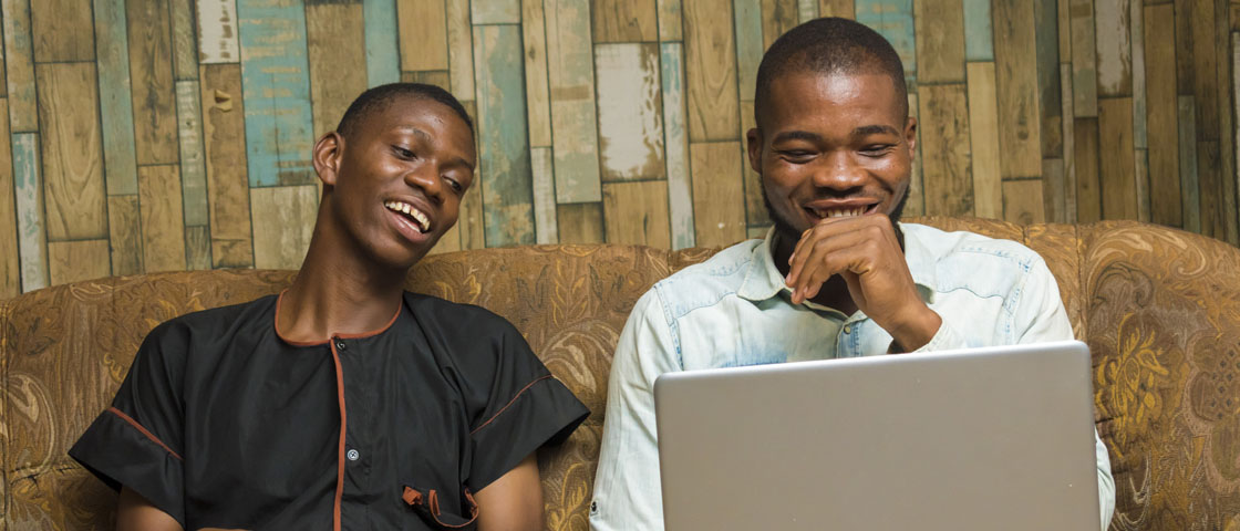 Two people sit on a couch while looking at a laptop computer screen