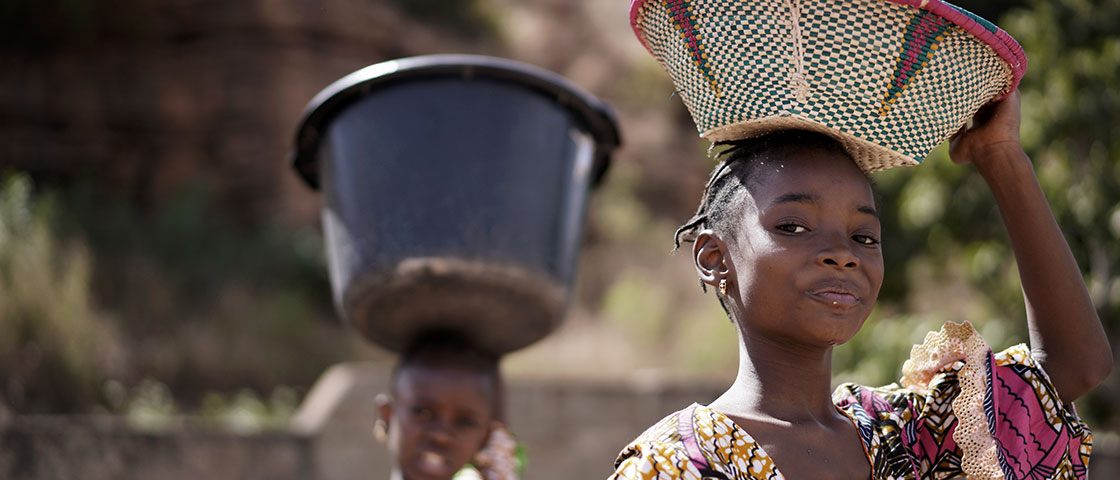 Two African Girls Carrying Heavy Items On Their Head